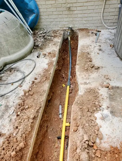 Yellow gas line laid in a trench cut through concrete beside a house.