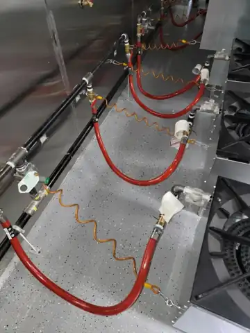 A commercial kitchen gas manifold with red flex connectors under a cook line.
