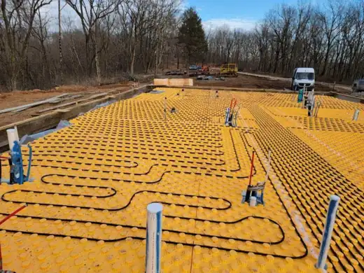 Radiant floor heating tubing laid in a yellow panel grid across a slab before the pour
