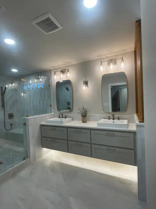 A finished primary bathroom with a floating double vanity, brass fixtures and a walk-in glass shower