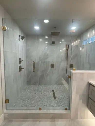 A walk-in glass shower with a rain head, linear drain and pebble floor.