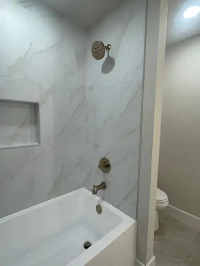 A tub and shower in marble-look tile with brushed-gold trim.