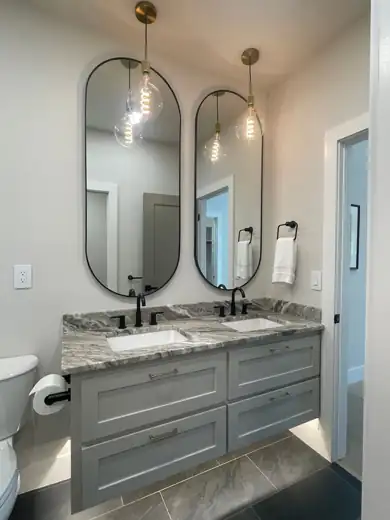 A double vanity with two pill mirrors, pendant lights and black faucets.