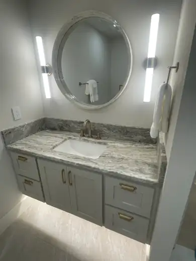 A floating vanity with a round mirror, LED strips and under-cabinet glow.