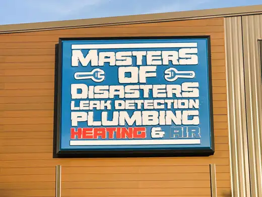 The Masters of Disasters building sign: a blue panel with the white stencil wordmark Masters of Disasters Leak Detection Plumbing and red Heating and Air