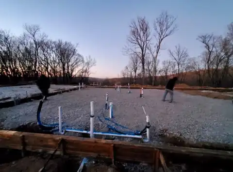 Under-slab plumbing rough-in on a gravel pad at dusk.