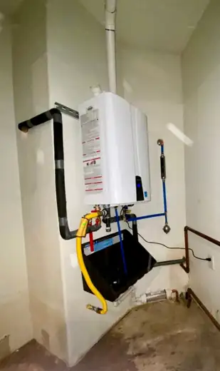 A tankless heater mounted in a utility room with black and yellow gas piping.