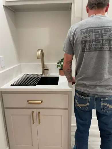 A crew member in a company shirt beside a finished laundry sink install.