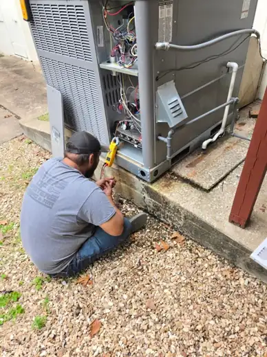 HVAC technician seated at a packaged unit with gauges and the panel open