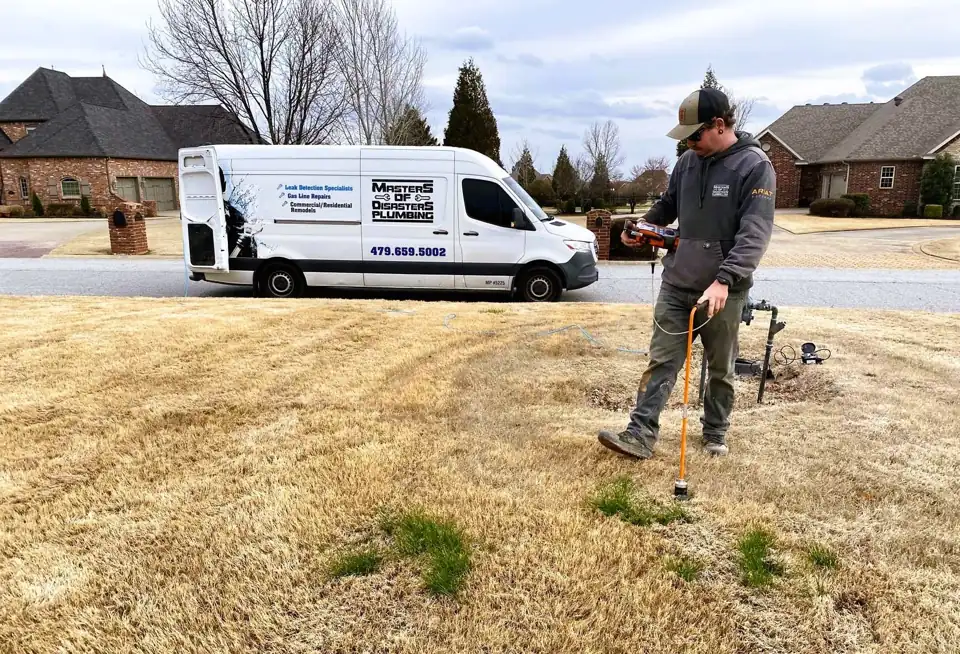 A Masters of Disasters technician walking a winter lawn with an orange ground-listening leak locator, the company van parked at the curb behind him