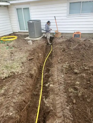 A yellow water line laid in a fresh trench running across a back yard to a house